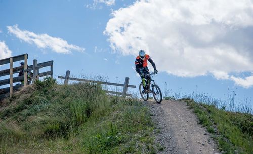 Rear view of man riding bicycle on field against sky