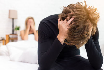 Tensed man with girlfriend sitting on bed at home