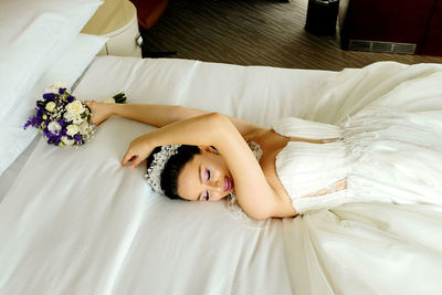 High angle view of bride holding bouquet while lying on bed