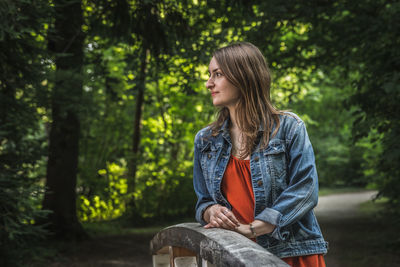 Young woman looking away while standing by railing against trees in forest