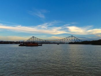 View of suspension bridge over river against cloudy sky