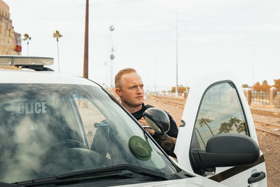 Horizontal image of white male caucasian police officer standing in the door opening of his trooper