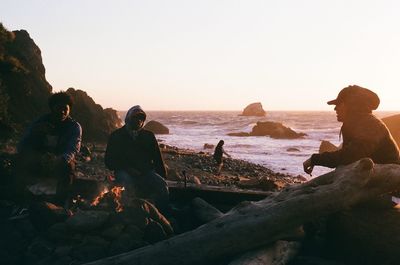 People standing on rock by sea against clear sky