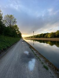 Road by trees against sky during sunset