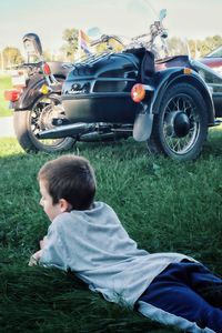 Boy lying on grassy field by parked motor scooter at park