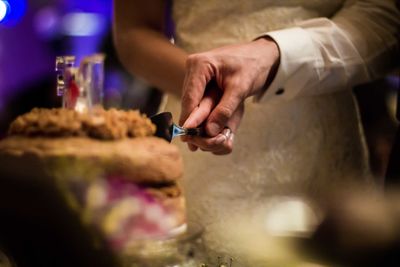 Midsection of wedding couple cutting cake during party