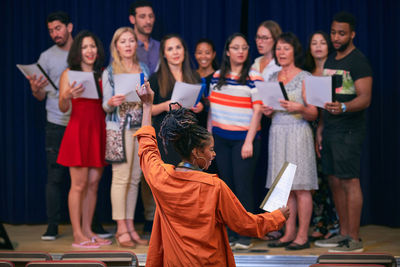 Young female conductor directing choir on stage in auditorium