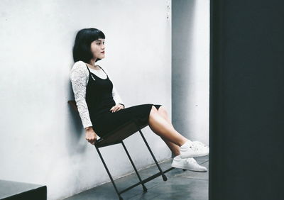 Young woman sitting on chair against wall