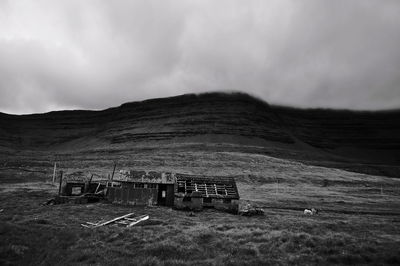 Broken hut on field with plateau in background against cloudy sky