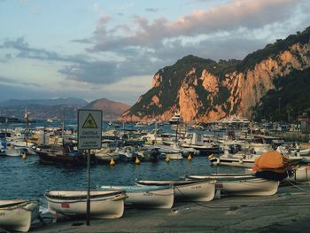 Boats moored on sea by mountain against sky