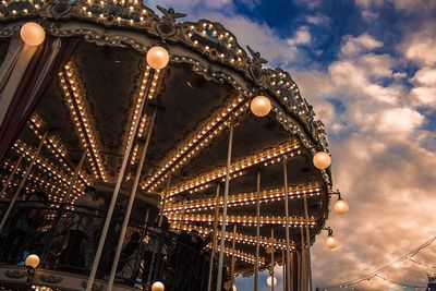 Low angle view of illuminated carousel against cloudy sky during sunset