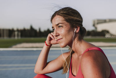 Thoughtful female athlete listening music while sitting on sports track