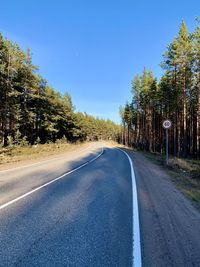 Empty road along trees and against clear sky