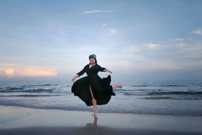 Rear view of woman standing at beach against sky