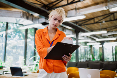 Portrait of young woman using mobile phone while standing in office