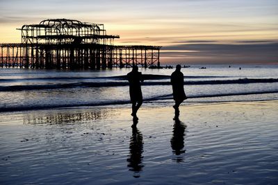 Silhouette men walking on beach against sky during sunset