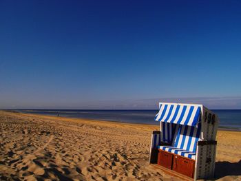 Hooded chairs on beach against clear blue sky