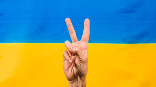 Hand in victory symbol with ukrainian flag for background