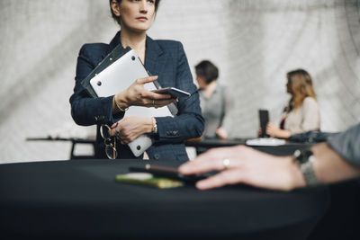 Midsection of businesswoman holding technologies while sitting at desk during meeting in office