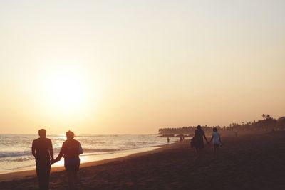 Silhouette people on beach against sky during sunset