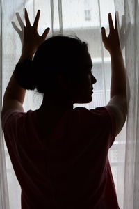 Rear view  of young girl standing against window at home