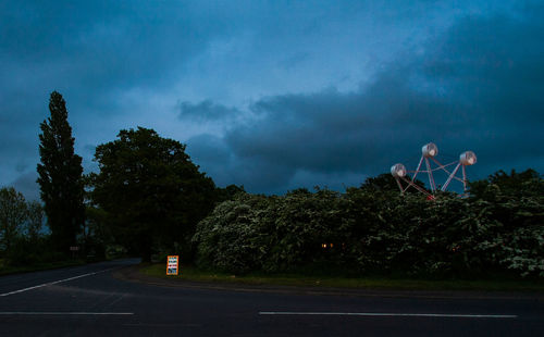 Road by trees against sky at dusk