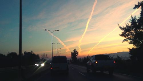 Cars on street against sky at sunset