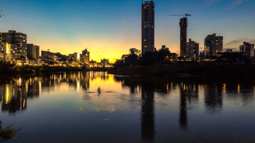 Scenic view of river by illuminated buildings against sky during sunset
