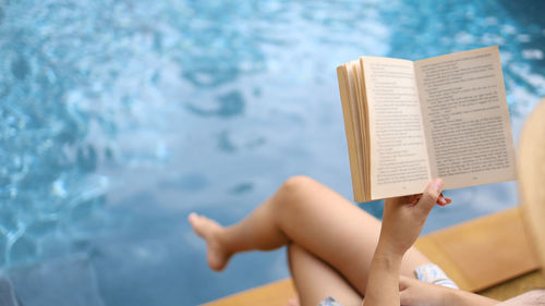 Low section of woman reading book against sea