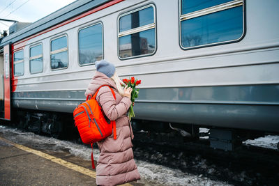 Girl on the platform of the station with a red backpack and a bouquet of tulip flowers