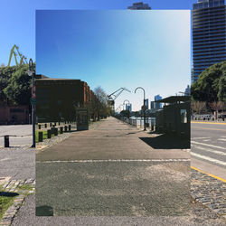 Empty road by buildings in city against sky