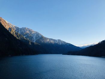 Scenic view of lake and mountains against clear blue sky