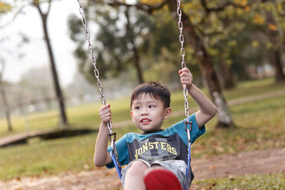 Portrait of boy sitting on swing at park