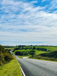 Empty road amidst field against sky