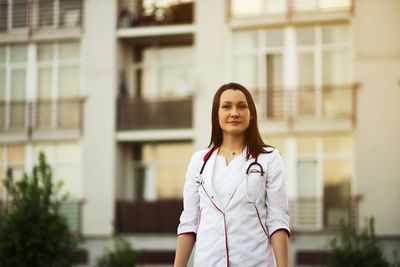 Portrait of young woman standing against building