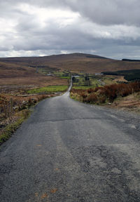 Country road along landscape against sky