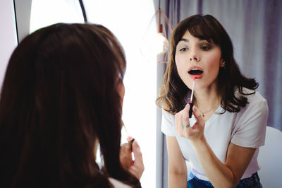 Close-up of young woman applying red lipstick in front of mirror at home