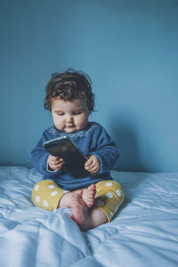 Cute girl using mobile phone while sitting on bed at home