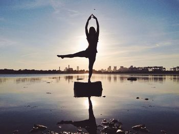 Silhouette woman doing yoga in sea against sky during sunset