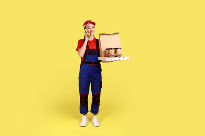 Portrait of woman holding gift box against yellow background