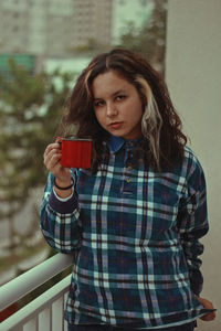 Portrait of young woman with coffee standing at balcony