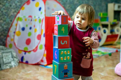 Cute baby girl playing with toy blocks at home