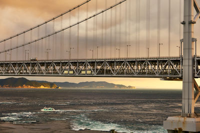 View of suspension bridge over sea against moody sky at sunset