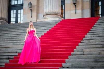 Female model wearing pink evening gown while standing on steps