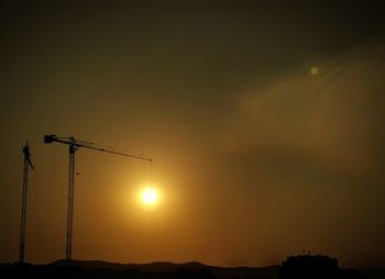 Low angle view of silhouette cranes against sky during sunset