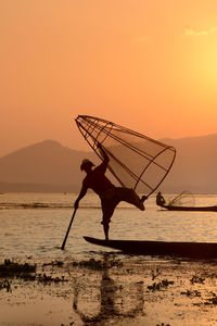 Fisherman fishing in lake with conical fishing nets during sunset
