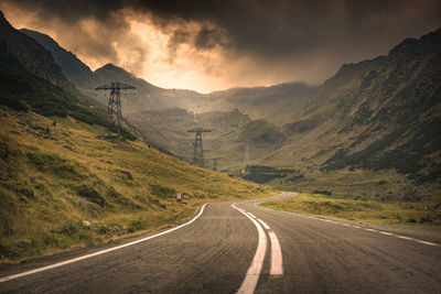 Empty road leading towards mountains against cloudy sky