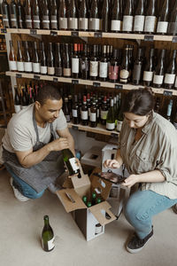 Male and female owners checking inventory of bottles while crouching in wine store