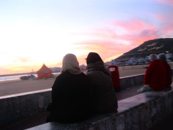 Rear view of couple sitting against sky during sunset