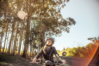 Young woman in jacket riding motorcycle on road